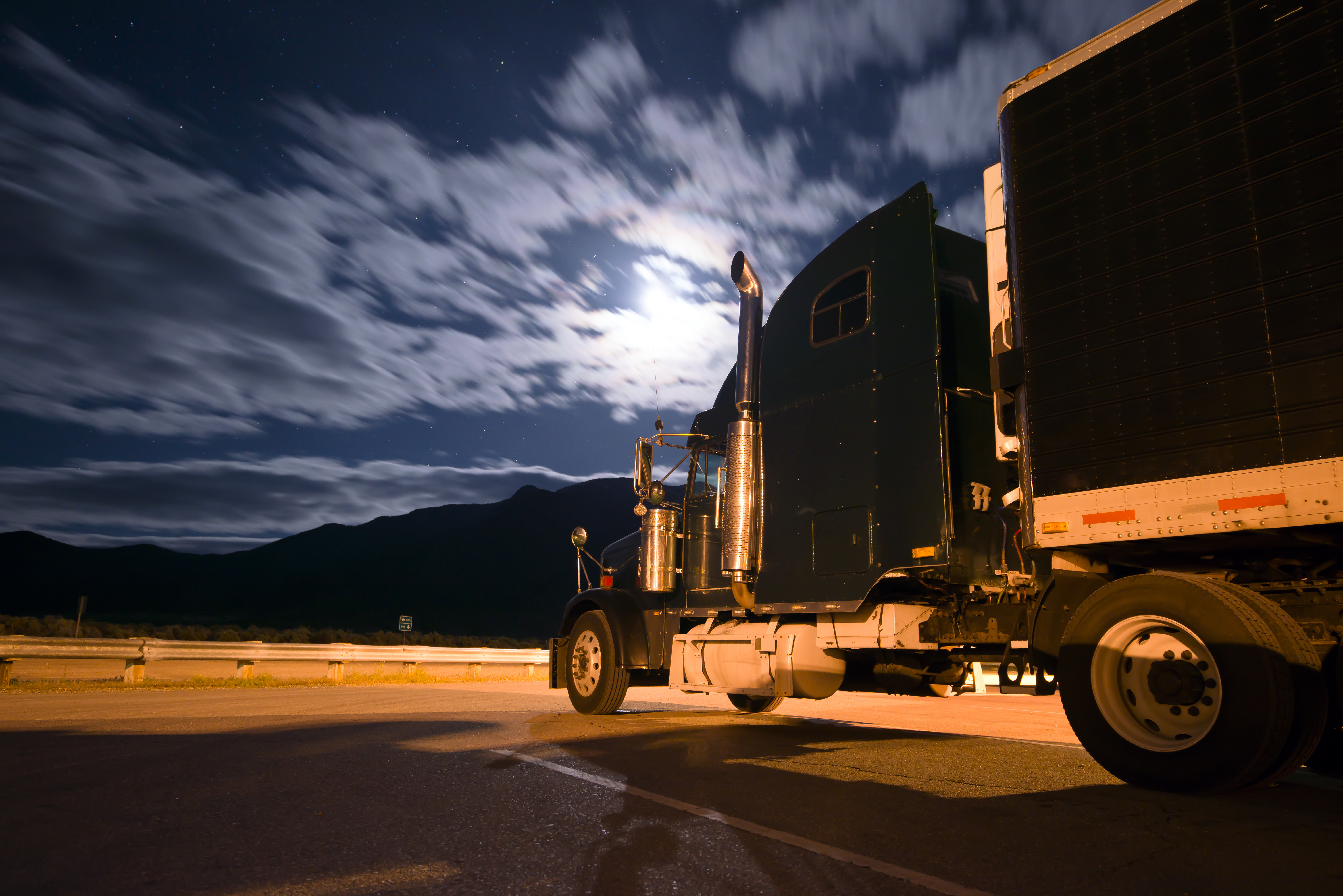 Dark semi truck reefer in night light with moony clouds